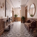 An elegant interior hallway with a black and white patterned tile floor, warm wood wainscoting, wall sconces, a large round mirror, and a carved wooden bench with cushions.