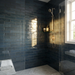 Modern bathroom with dark blue tiled walls, gold fixtures, and a window.